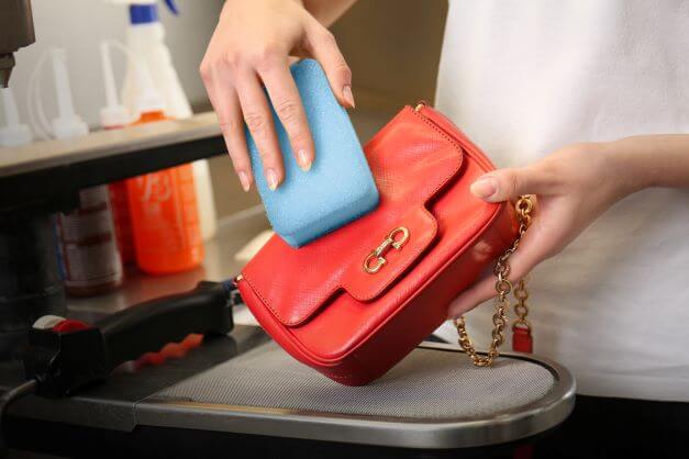 clean leather handbag with damp sponge