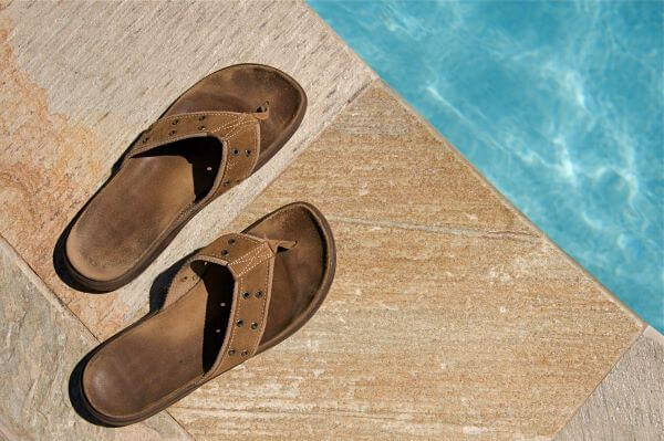 Old brown leather flip flops next to a swimming pool