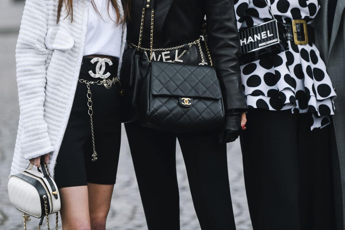 3 women earing designer handbags with big logos showing it is from Chanel